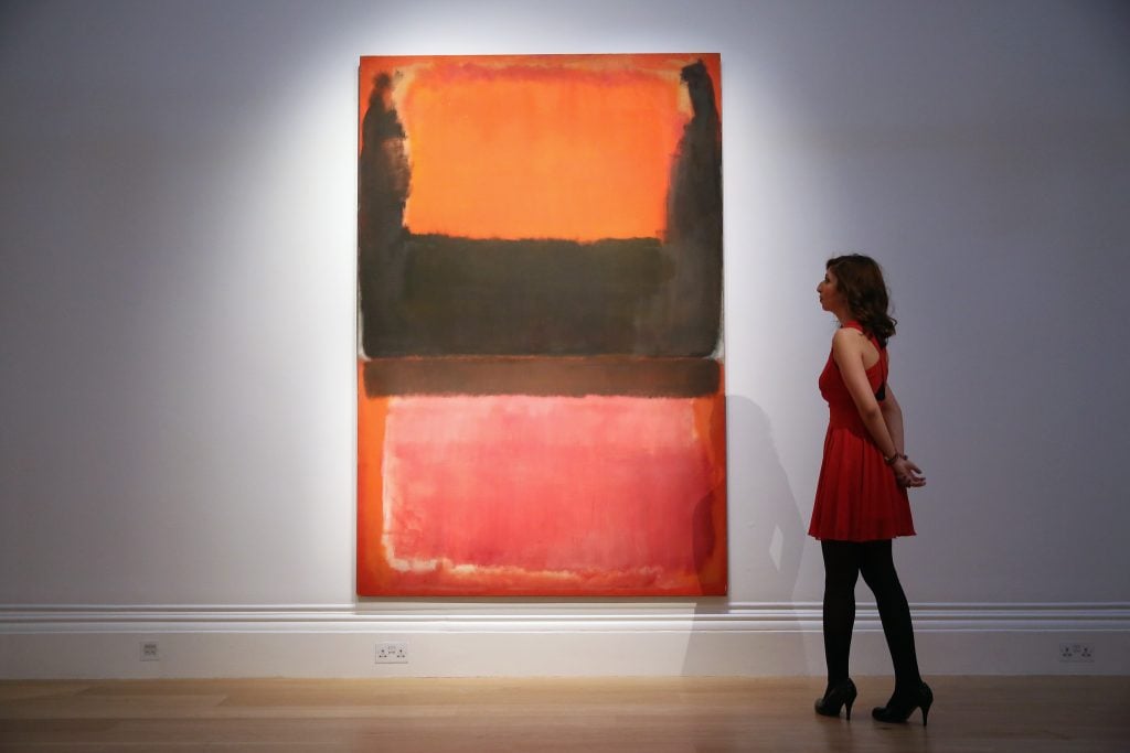 Woman in red dress observes Mark Rothko painting of dark horizontal blocks over glowing red-orange fields.