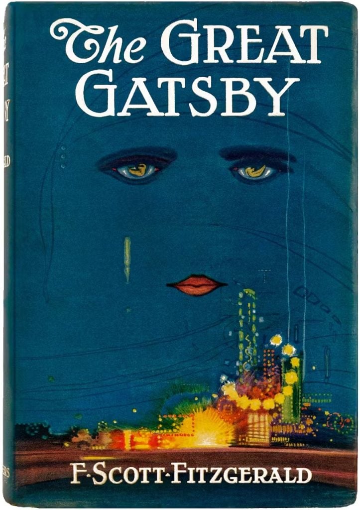a copy of the great gatsby book with a deep blue dust jacket with a abstract face hovering in the sky above bright flickering lights