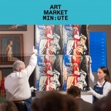 Art handlers hold up an artwork at the head of an auction room
