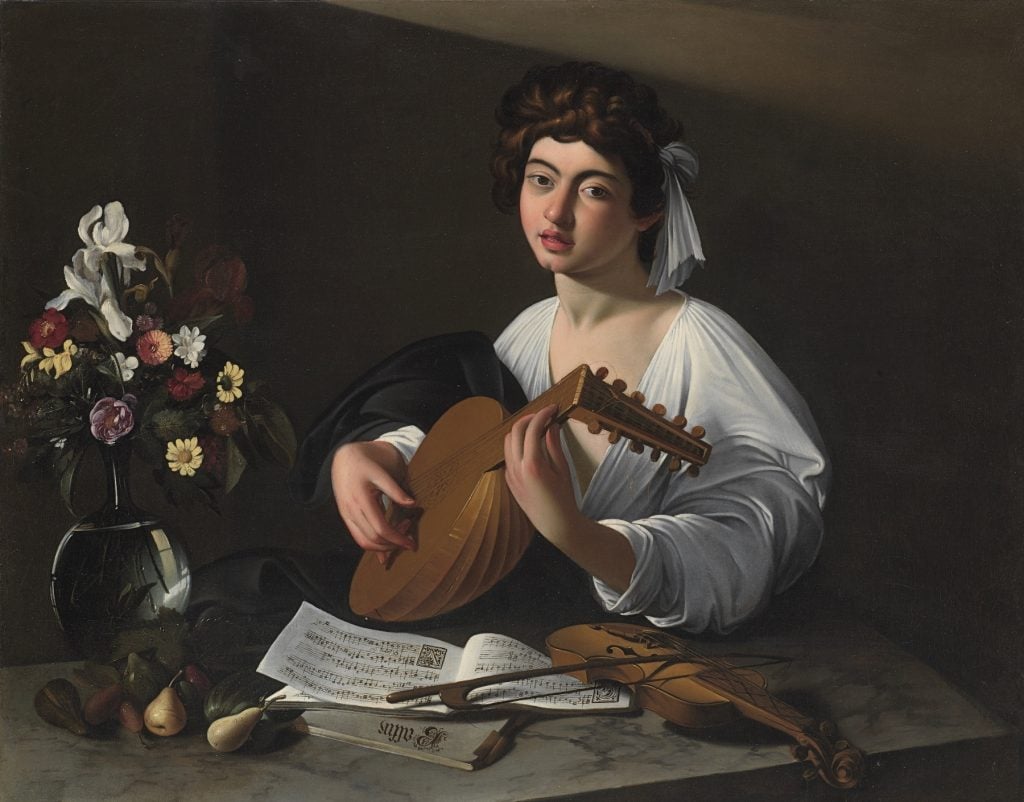 a painted scene in which a young boy plays a lute, he wears a loose and low-cut white shirt and he is at a desk with a vase of flowers, some fruit, and an open book of music