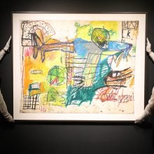 Two attendants hold up a colorful abstract oil stick painting