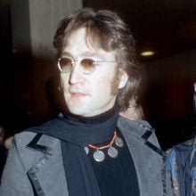 a man with a necklace and a coat and glasses