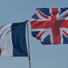 The Union Jack on the right and French flag on the left against a blue sky.