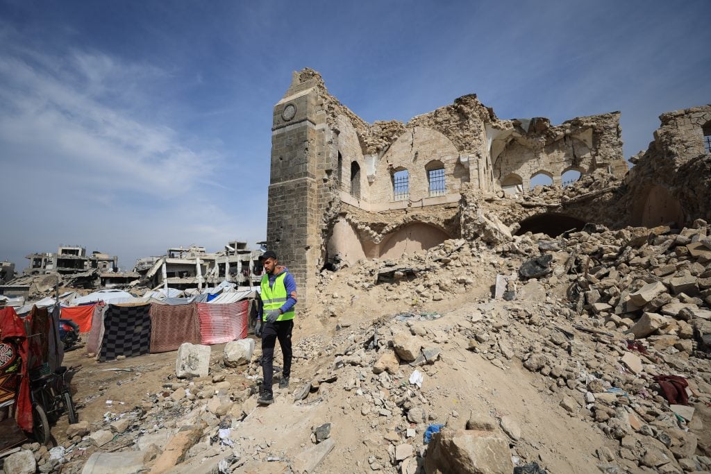 Ruins of Gaza’s historic Pasha’s Palace with collapsed stone walls, rubble, and man walking nearby.