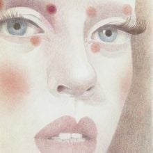 A close-up drawing of a woman’s face by Sarah Ball, titled Emma (2025), shown at Stephen Friedman Gallery. The portrait, rendered in delicate colored pencil, highlights blue-gray eyes, full lips, and flushed cheeks, with red circular markings on the forehead and below the eyes. The detailed eyelashes and subtle shading emphasize both natural beauty and stylized features.