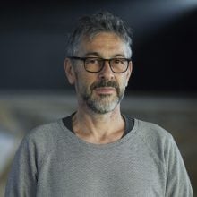 Portrait of a man wearing glasses and a gray sweater, standing in soft indoor lighting.