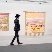 A person dressed in a slim fitting suit walks past colorful artworks on a white wall