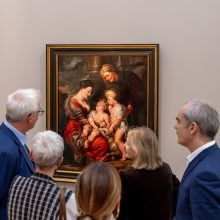 A group of people stand looking at an old master painting depicting four figures