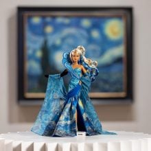 a barbie doll in a blue dress with a painting behind her