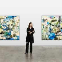 a woman in black poses in front of two abstract paintings