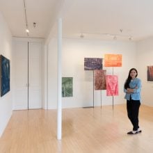 a woman in a blue top and black pants stands in an art gallery
