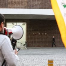 a protestor with a bull horn stands outside of an art gallery