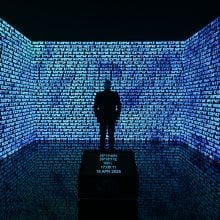 A person immersed in a digital installation, surrounded by screens showing digits lit in blue in a dark room.