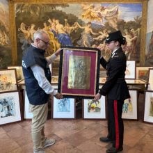 Two police officers hold up an artwork for the camera, with many other artworks on display behind them