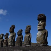 A row of moai statues on Easter Island, standing on a stone platform against a clear blue sky.