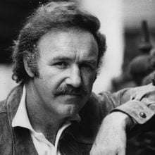 A black-and-white portrait of Gene Hackman, looking directly at the camera with a serious expression.