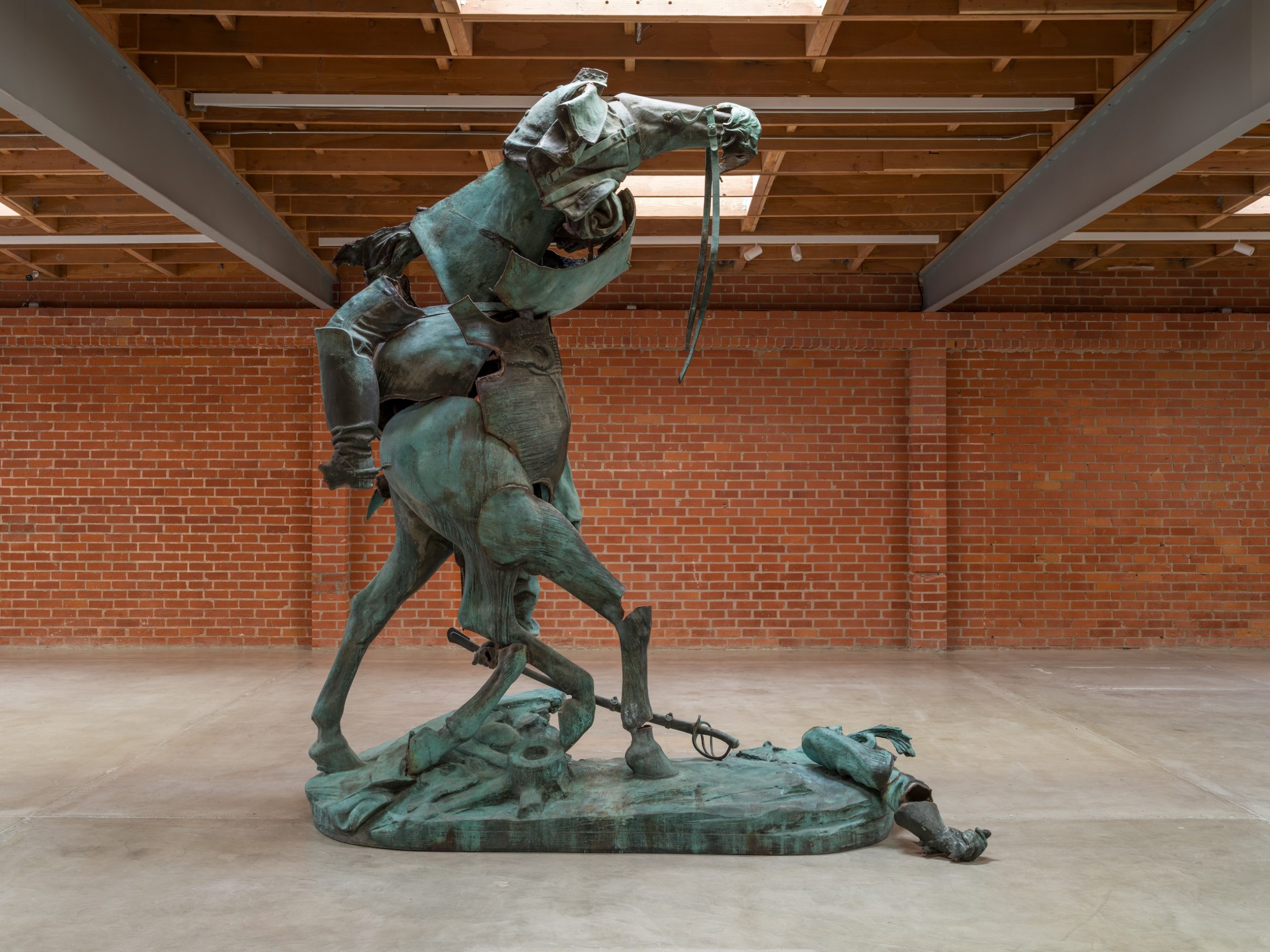 A photo shows a large art gallery with a brick wall. At its center stands an 11-foot-high bronze artwork created by rearranging the parts of an equestrian monument