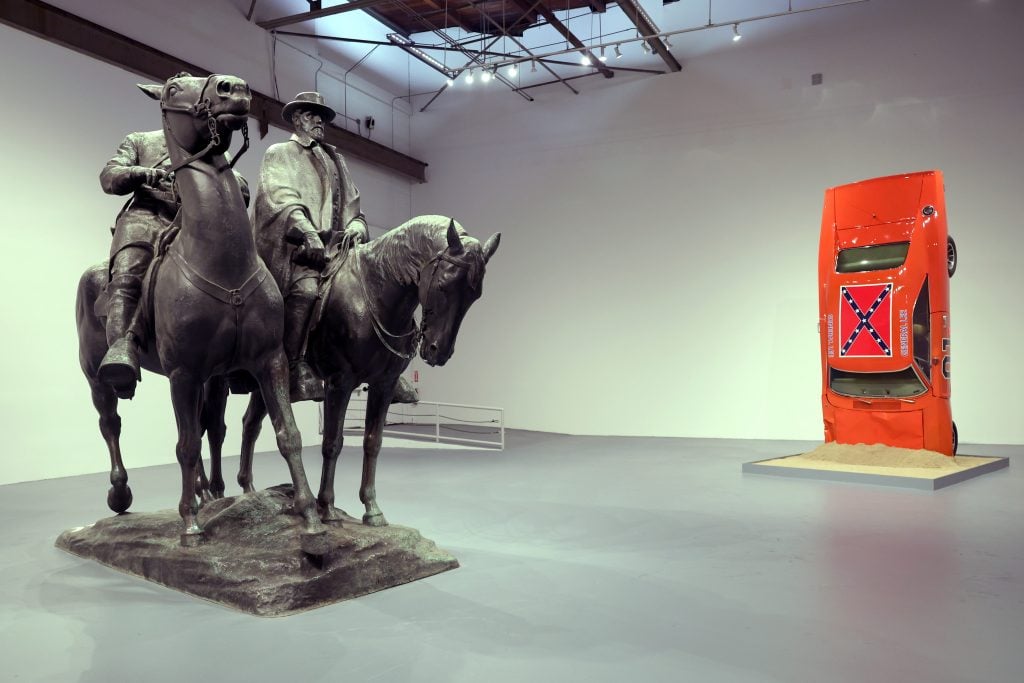 A photo shows an art gallery with a bronze monument showing two men on horseback and, nearby, a replica of the car named the "General Lee," from the television show "the Dukes of Hazzard"