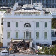 Excavators demolish lower section of White House East Wing while workers oversee debris and construction barriers.