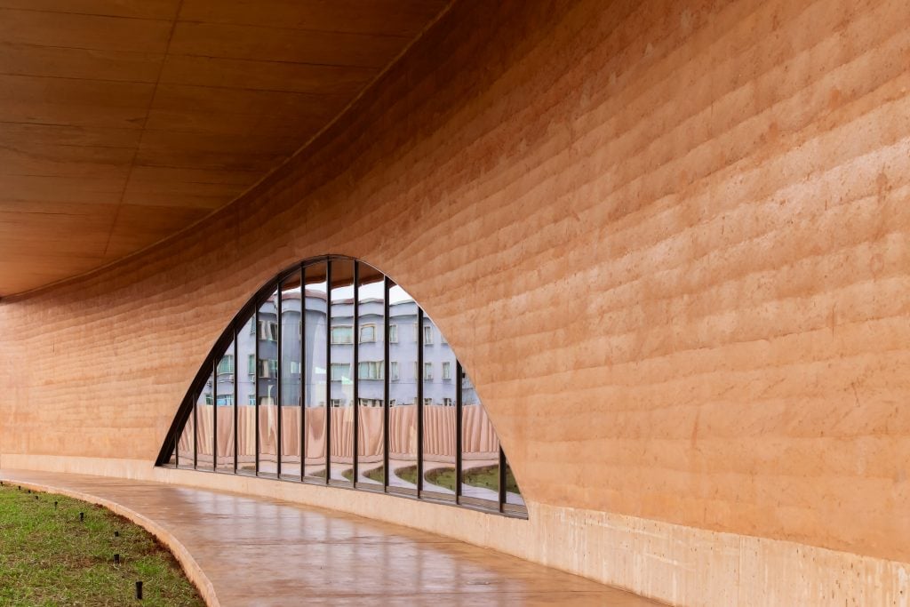 Curved rammed-earth wall with arched window and polished concrete walkway in contemporary architectural design.