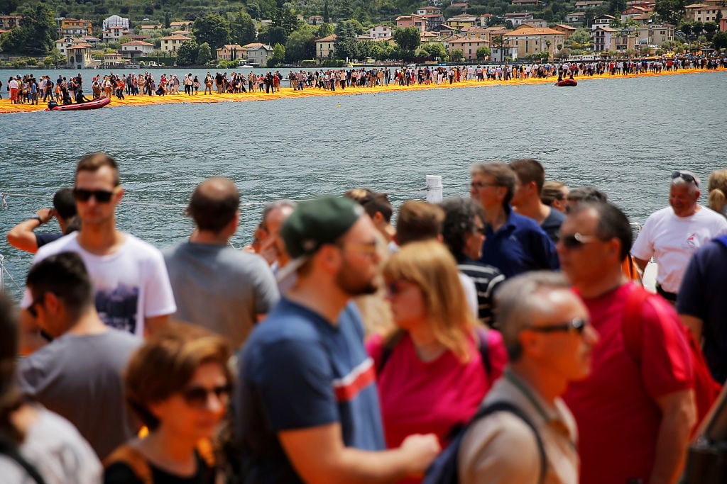 People walk on the monumental installation entitled 'The Floating Piers' created by artist Christo Vladimirov Javacheff on Iseo Lake, in northern Italy, on June 18, 2016. Some 200,000 floating cubes create a 3-kilometers runway connecting the village of Sulzano to the small island of Monte Isola. Courtesy of MARCO BERTORELLO/AFP/Getty Images.